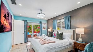 A bedroom with a bed, a nightstand, a lamp, a window with curtains, and a view of an outdoor pool area. - Waterfront w/ Htd Pool, Tiki Hut, Billards, & Bar (Boynton Beach)