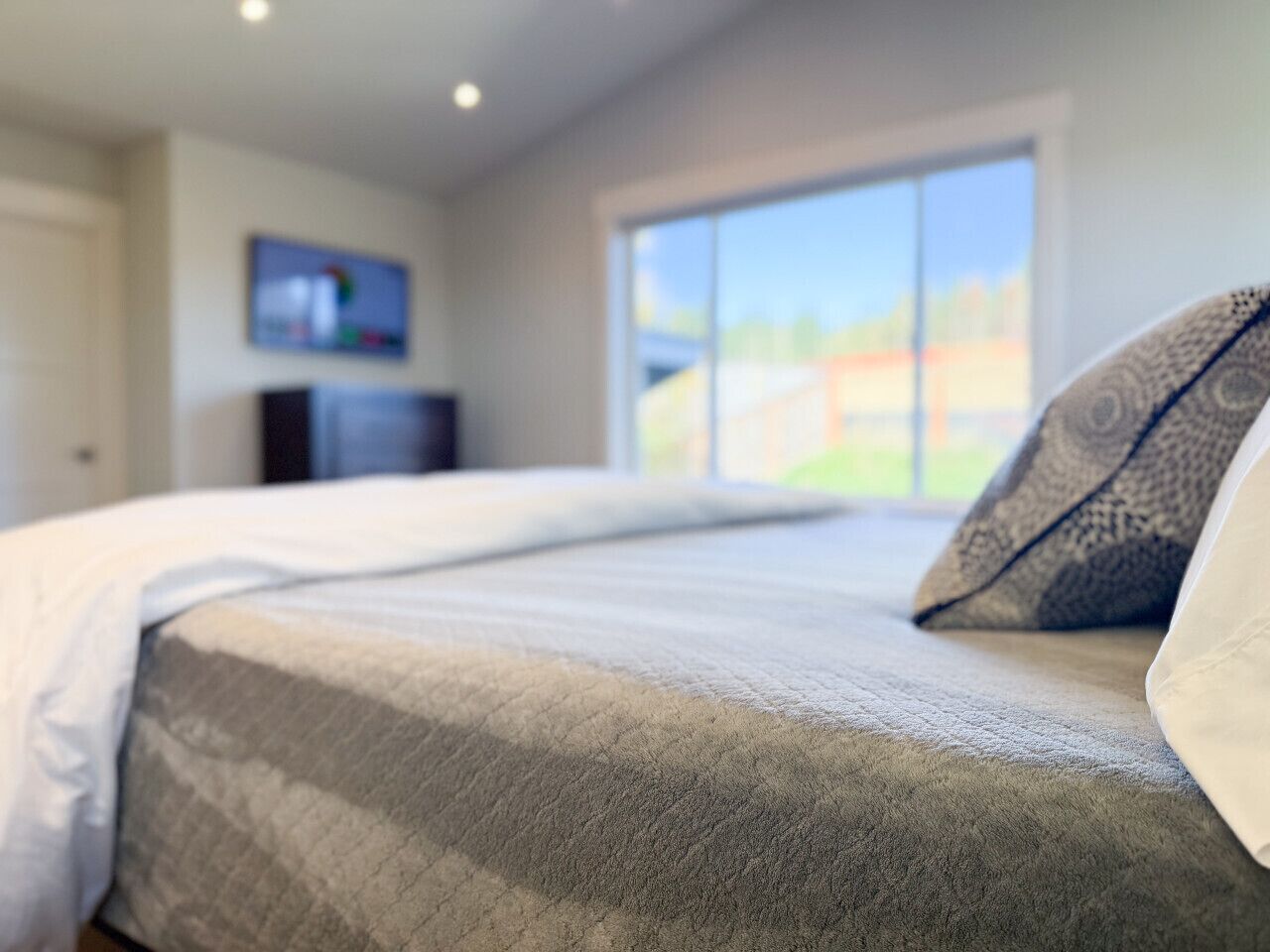 A bedroom with a large bed, a television on the wall, and a window with a view of the outdoors.