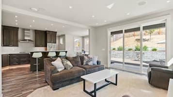 A modern living room with a sofa, a coffee table, and a view of the backyard through large sliding glass doors.