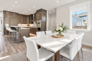 A modern kitchen with dark wood cabinets, stainless steel appliances, and a white dining table with six chairs.