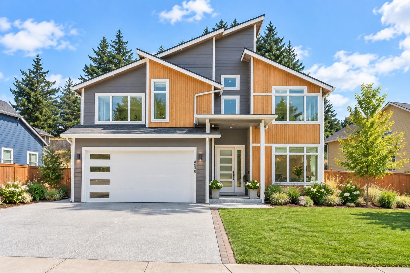 A modern two-story house with a garage, large windows, and a well-maintained lawn.