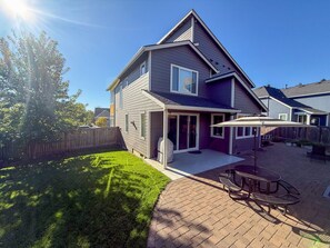Ein zweistöckiges Haus mit einer Terrasse, einem überdachten Sitzbereich und einem eingezäunten Garten.