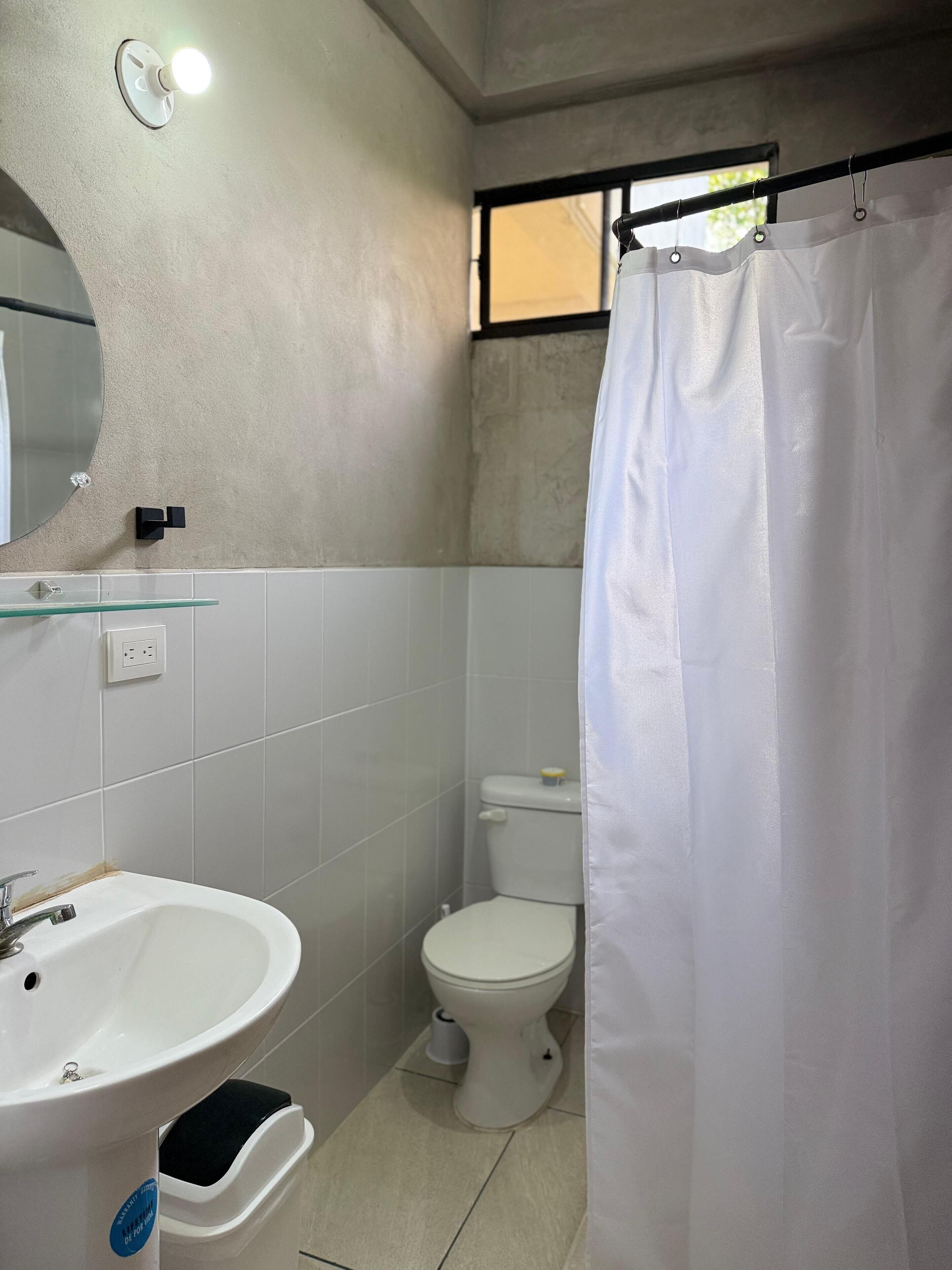 Une salle de bain avec un lavabo blanc, un miroir, des toilettes et un rideau de douche.
