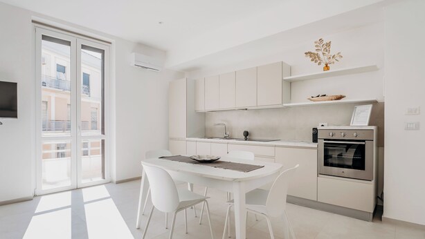 A modern kitchen with white cabinetry, a dining table with chairs, and a built-in oven. - Hieron II (Siracusa)