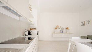 A modern kitchen with white cabinetry, a stainless steel cooktop, and a white dining area with a table and chairs. - Hieron II (Siracusa)