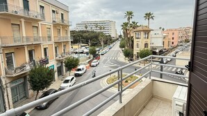 A balcony with a view of a city street, buildings, and palm trees. - Hieron II (Siracusa)