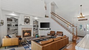 Ein großzügiges Wohnzimmer mit Kamin, Ledersofas, Fernseher und einer Treppe, die zu einer zweiten Etage führt.