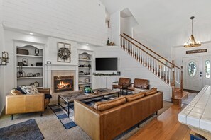 A spacious living room with a fireplace, leather sofas, a TV, and a staircase leading to a second floor.