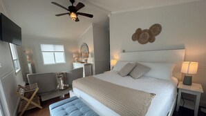 Un dormitorio con cama, mesitas de noche, una silla, ventilador de techo y espejo adosado a la pared.