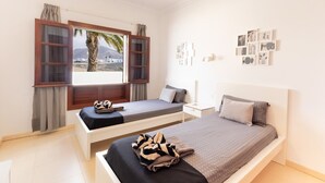 Een slaapkamer met twee bedden, een raam met gordijnen, een plafondventilator en kunst aan de muur.