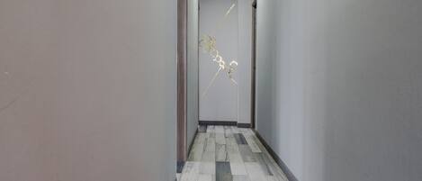 A hallway with a patterned floor, a framed artwork on the wall, and a light fixture on the ceiling.