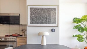 A modern kitchen with a round dining table, wooden chairs, a pendant lamp, and a large abstract painting on the wall.