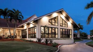 A modern two-story house with large windows, a sloped roof, and a well-maintained lawn. - Countryside Golf and Country Club 2bed 2bath all new Clubhouse & facilities (Naples)