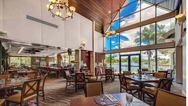 A spacious restaurant with high ceilings, large windows offering a view of the outdoors, and a variety of seating arrangements. - Countryside Golf and Country Club 2bed 2bath all new Clubhouse & facilities (Naples)