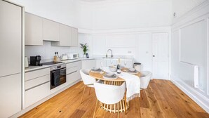Een moderne keuken met witte kasten, een eethoek met een ronde tafel en witte stoelen, en een houten vloer.