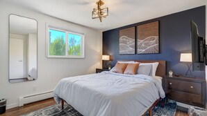 Une chambre à coucher avec un lit, des tables de chevet, un miroir et des œuvres d’art accrochées au mur.