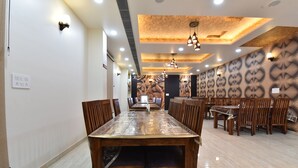 A spacious dining area with a long wooden table and chairs, recessed ceiling lights, and patterned wall decor. - INDRA PALACE (Jaipur)