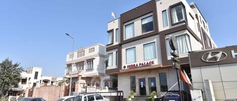 A modern hotel with a sign reading "INDRA PALACE." There are cars parked in front, and the building has multiple floors with large windows.