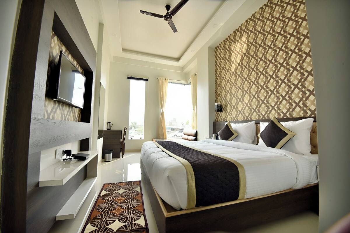 A modern hotel room with a large bed, a flat-screen TV, a ceiling fan, and a patterned wall.