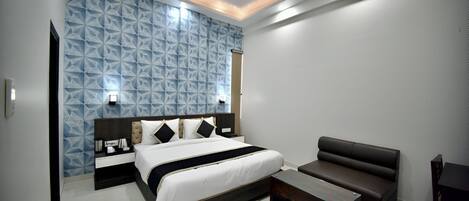 A modern bedroom with a geometric-patterned wall, a large bed, a dark brown sofa, and a small table.