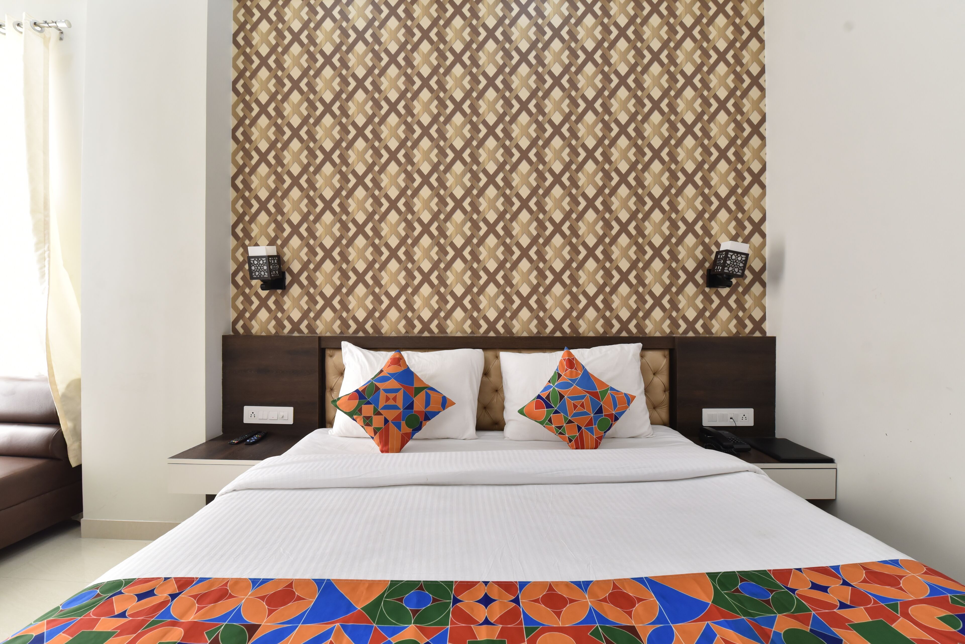 A hotel room with a bed, two nightstands, a patterned headboard, and a colorful bedspread.