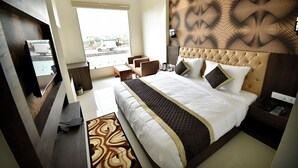 A modern hotel room with a large bed, a TV, a desk, and a view of the street. - INDRA PALACE (Jaipur)