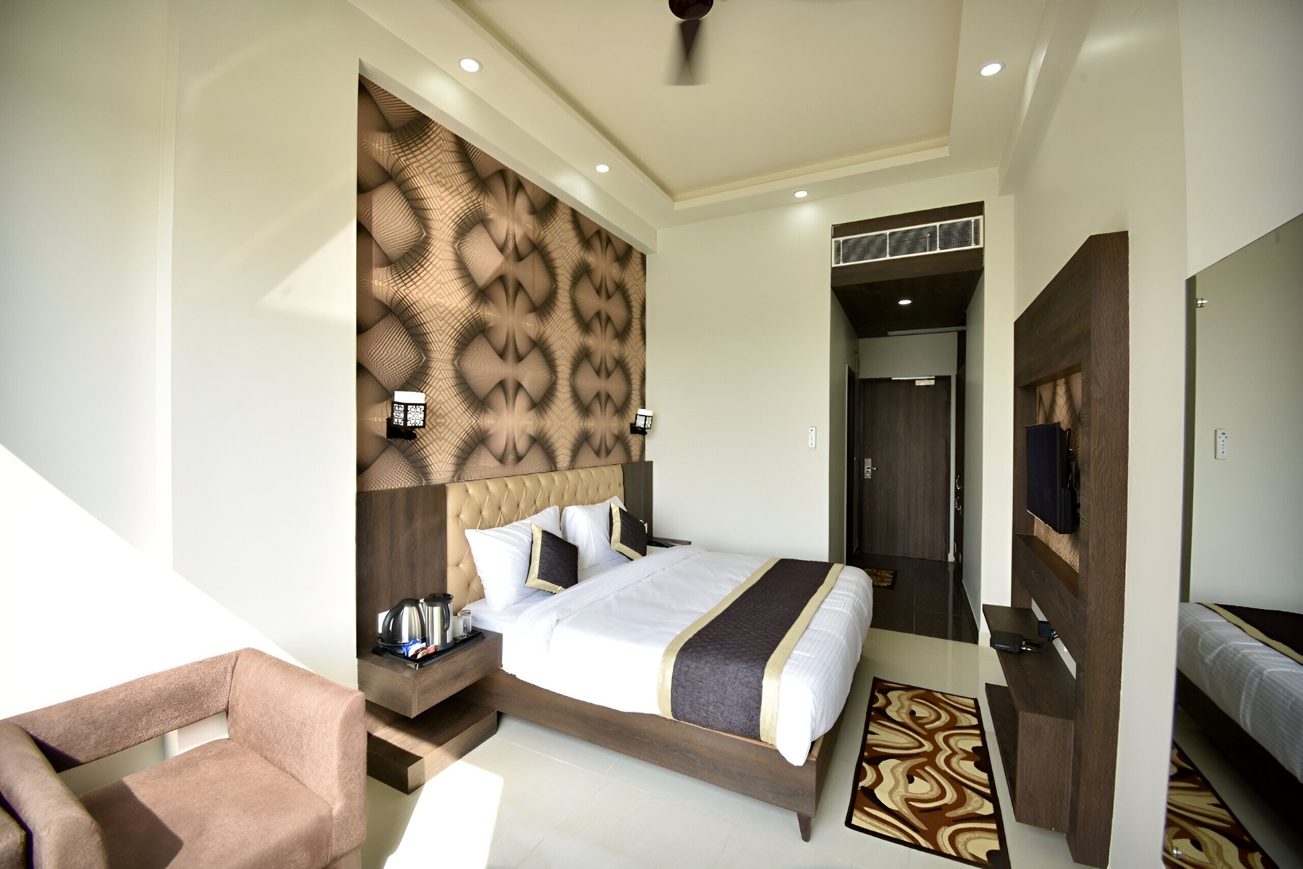 A modern hotel room with a large bed, a sofa, a desk with a lamp, and a television.