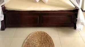 Un lit simple avec un baldaquin, une table de chevet et un panier en osier posé sur le sol.
