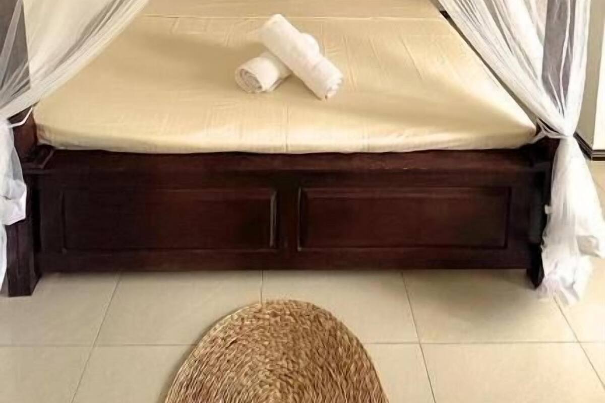 Un lit simple avec un baldaquin, une table de chevet et un panier en osier posé sur le sol.