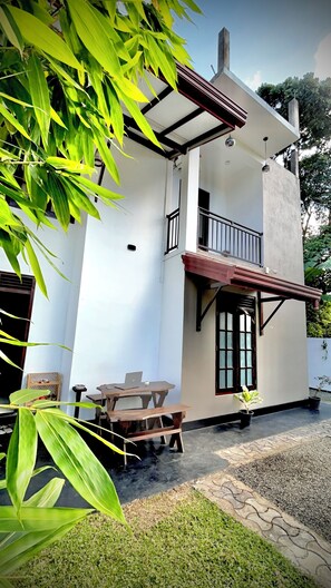 A two-story house with a balcony, a small patio with a table and chairs, and a garden area with a potted plant. - Casa Serendib Weligama  (Weligama)