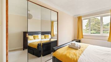 A modern bedroom with a large mirror, a bed with yellow bedding, a window with curtains, and a radiator.