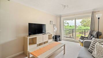 A living room with a TV, sofa, and a balcony with a view of greenery.