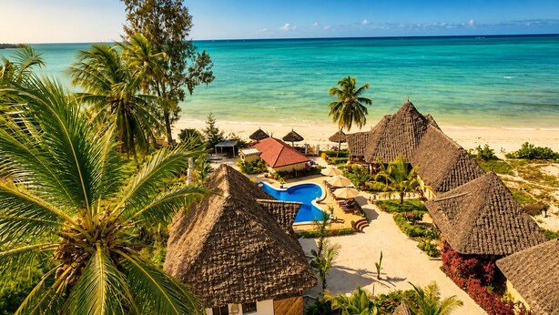 Um resort na praia com bangalôs de telhado de palha, piscina e vista para o oceano.
