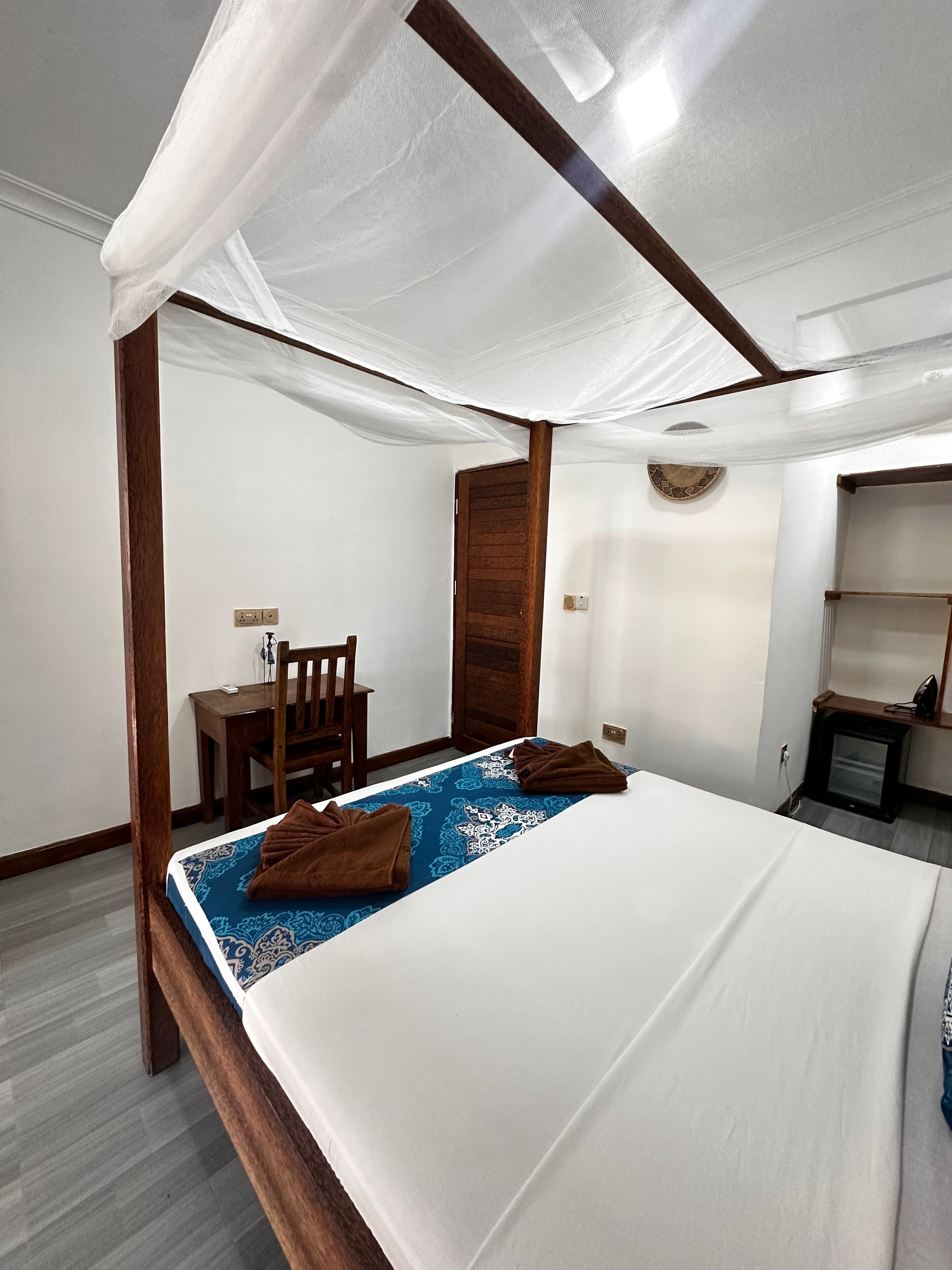 A bedroom with a four-poster bed, a wooden desk, and a small seating area.