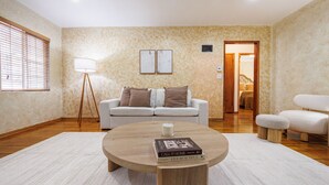 A living room with a round wooden coffee table, a white sofa with brown cushions, a floor lamp, and a door leading to another room.