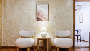 A room with two plush chairs, a small wooden table with a lamp, and a textured wall with a framed artwork.