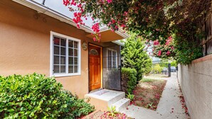A house with a front door, a window, and a small garden with flowers and shrubs.