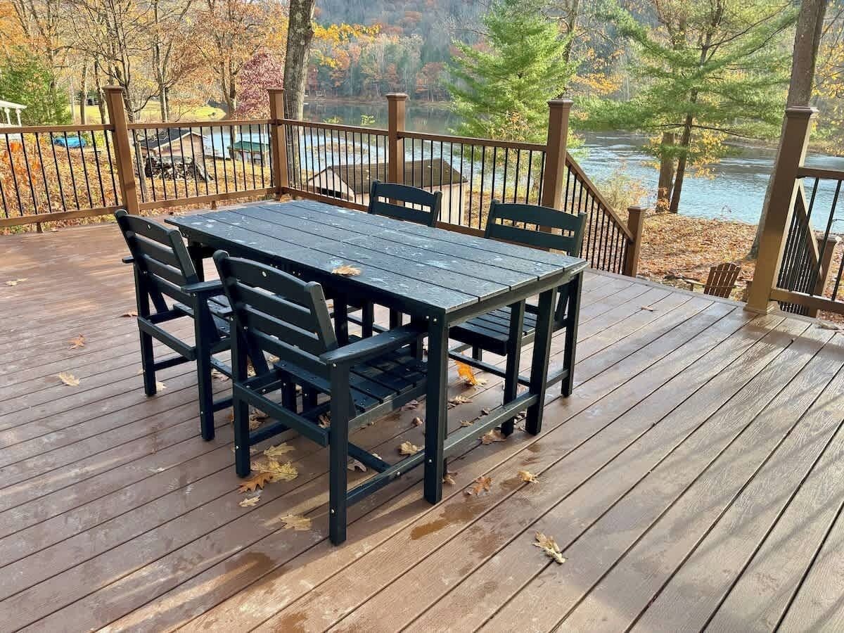Une terrasse en bois avec une table et des chaises, d’où l’on peut admirer une rivière et les couleurs automnales des arbres.