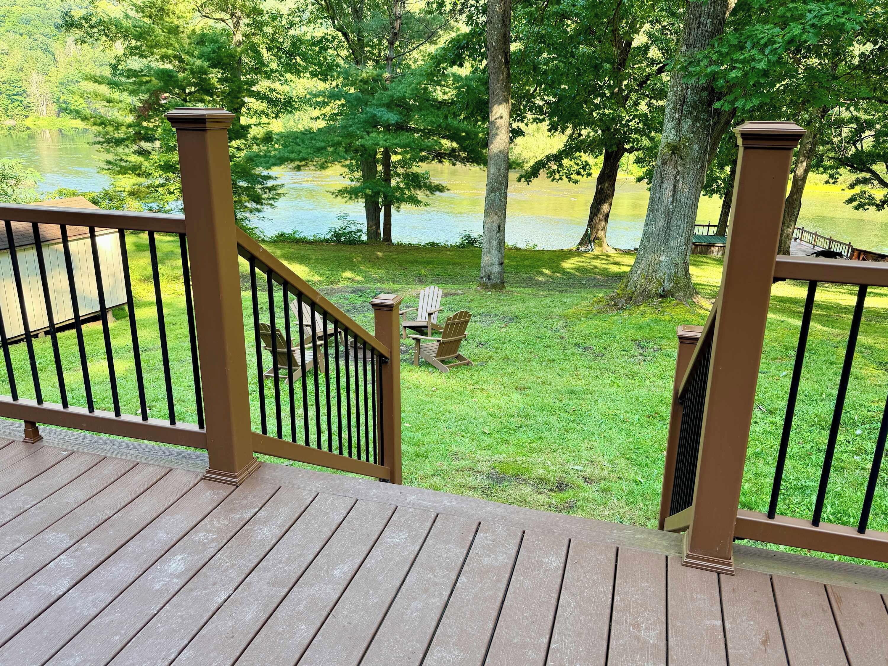 A wooden deck with a railing overlooking a grassy area with trees and a body of water.