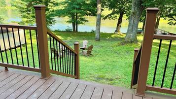 A wooden deck with a railing overlooking a grassy area with trees and a body of water.