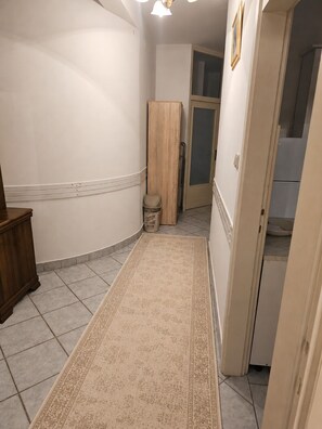 A hallway with a patterned rug, a wooden cabinet, a trash bin, and a door leading to another room. - Kiki- Emerald River Suite with Private Gardens in Center of Čapljina (Čapljina)