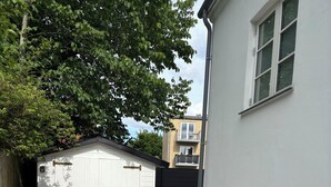 Ein von einer Mauer gesäumter Weg führt zu einem Gebäude mit weißer Fassade und einem Balkon mit einer Brüstung.