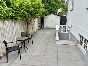 En uteplats med ett bord och stolar, ett vitt förråd och en grå byggnad.