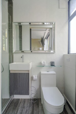 Un baño moderno con un lavamanos blanco, un estante de vidrio, un inodoro y un espejo grande.