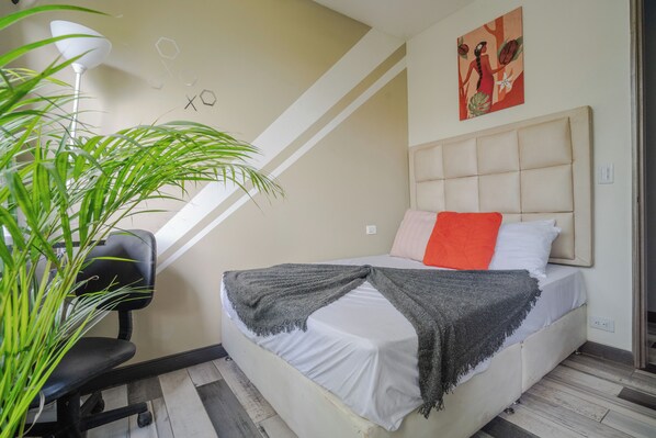 Un dormitorio con cama, escritorio, silla y planta en maceta.