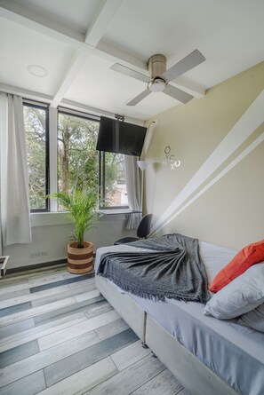 Un dormitorio con una cama, un ventilador de techo, una planta en maceta y una ventana con cortinas.