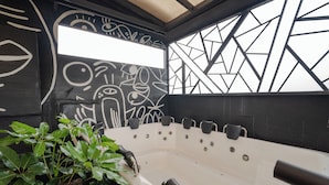 Et moderne badeværelse med et stort badekar, sort-hvid vægkunst og grønne planter.