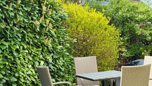 Eine Terrass mit Korbmöbeln, einem Tisch und einer Steinbordurierung.