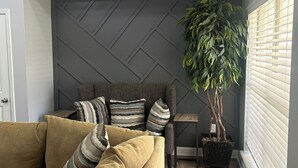A modern living room with a sectional sofa, decorative pillows, a potted plant, and a geometric wall panel. - Newly Remodeled Home with Full Deck and Gazebo. (Jackson)