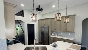 Een moderne keuken met een centraal eiland, roestvrijstalen apparatuur en hangende verlichting.